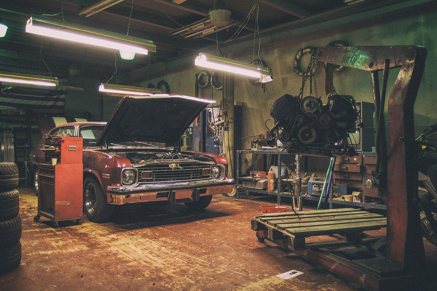 Working auto shop bay with vintage car, open hood, tool chest, and engine hoist